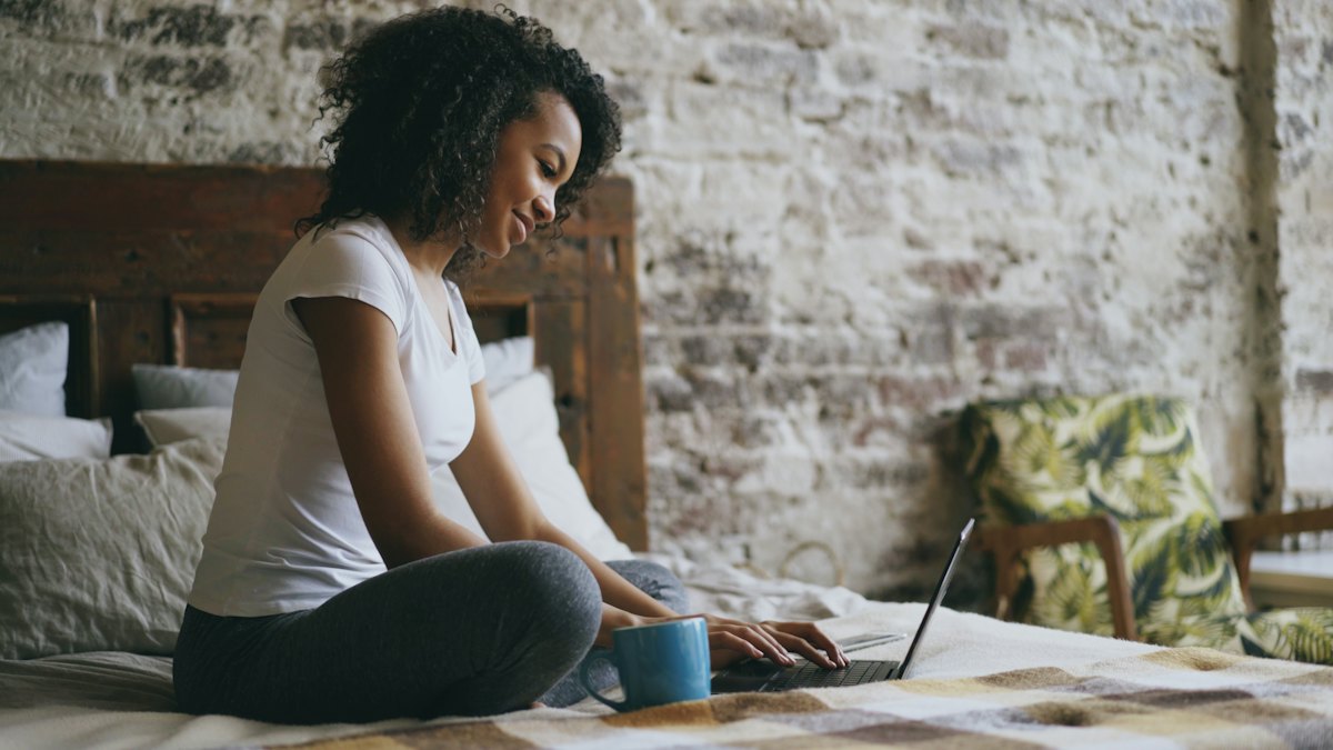 A woman sitting cross-legged on a bed working on a laptop