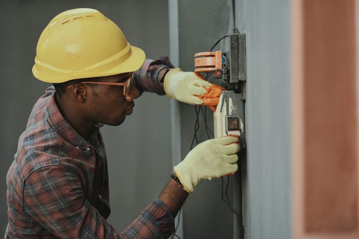 An electrician in a hard hat working on a wall panel