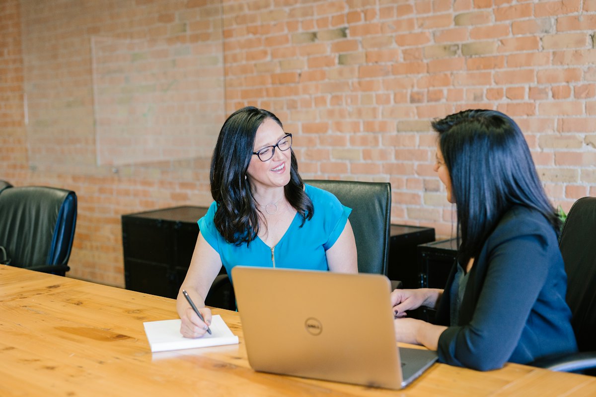 Two women talking across a table with a laptop open