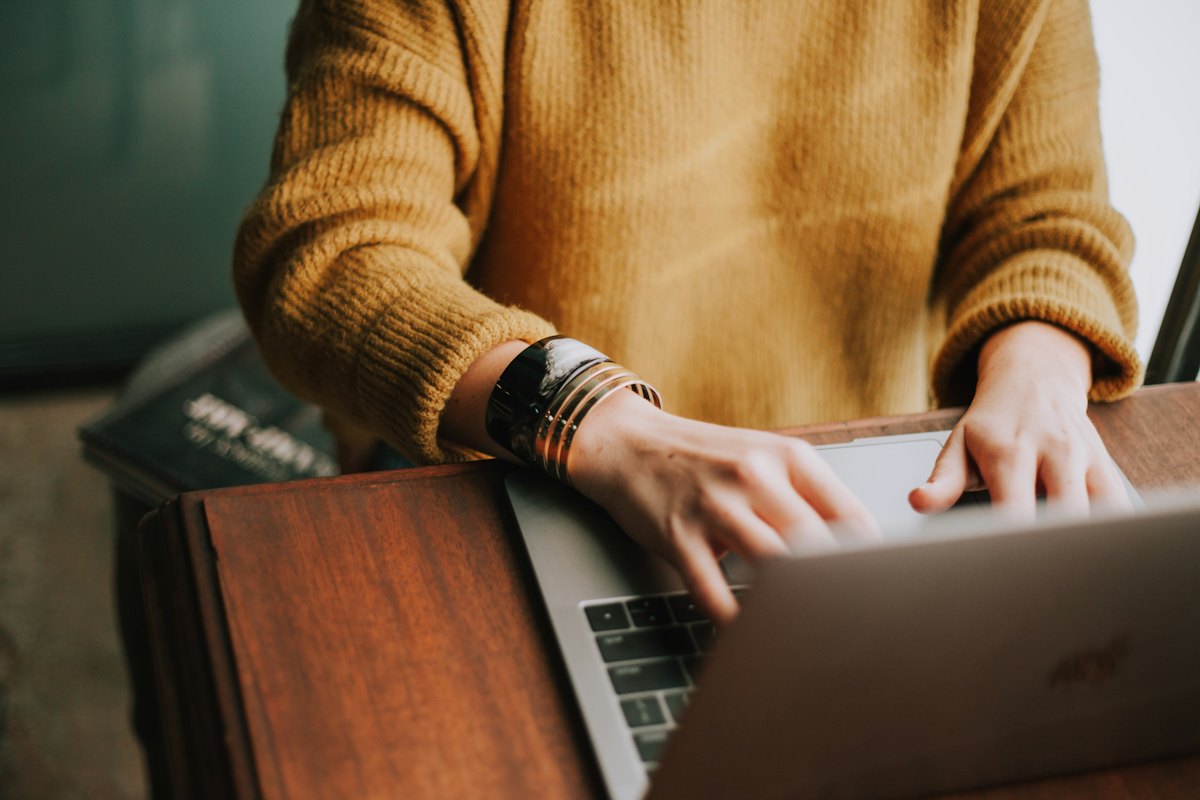 A person typing on a laptop on a wooden table