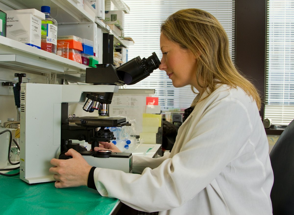 A researcher in a white coat working at a microscope