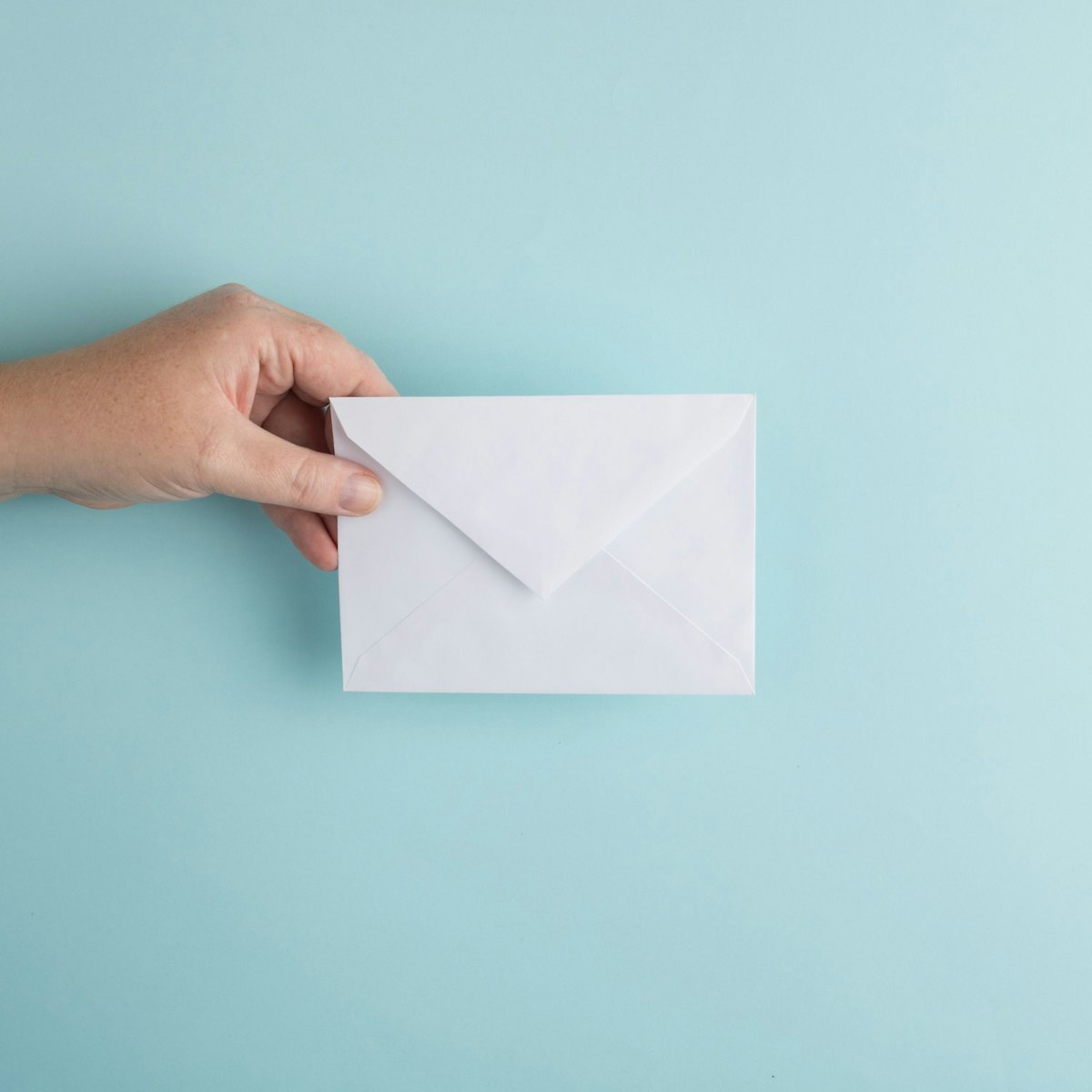 A hand holding a white envelope against a pale blue wall
