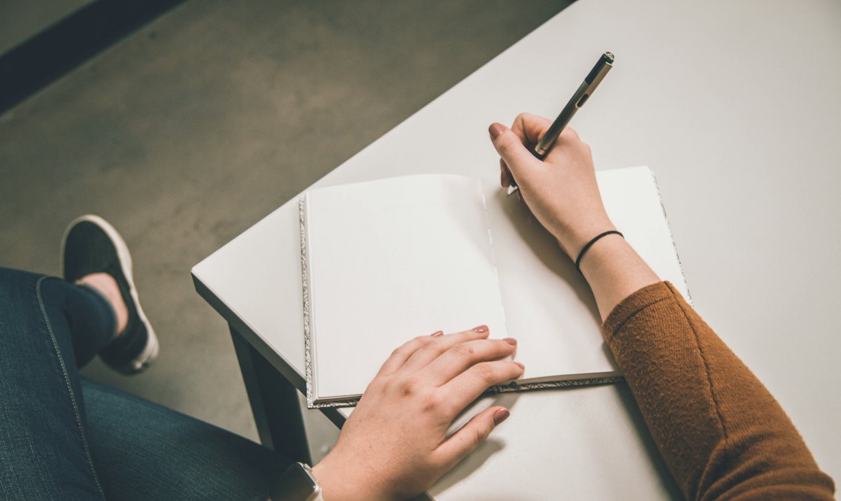 A hand writing with a pen in an open notebook