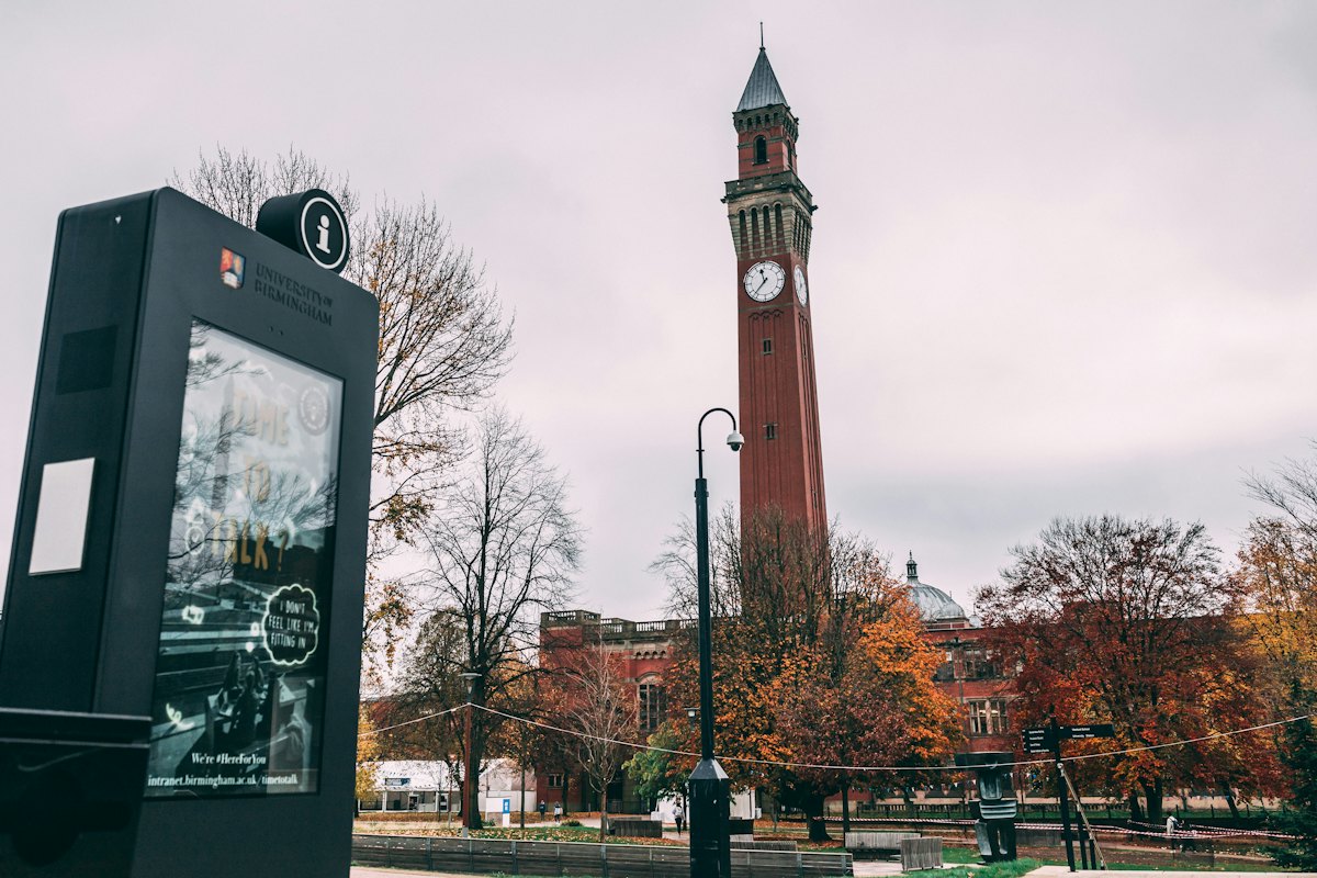 A brick clock tower behind autumn trees on a campus