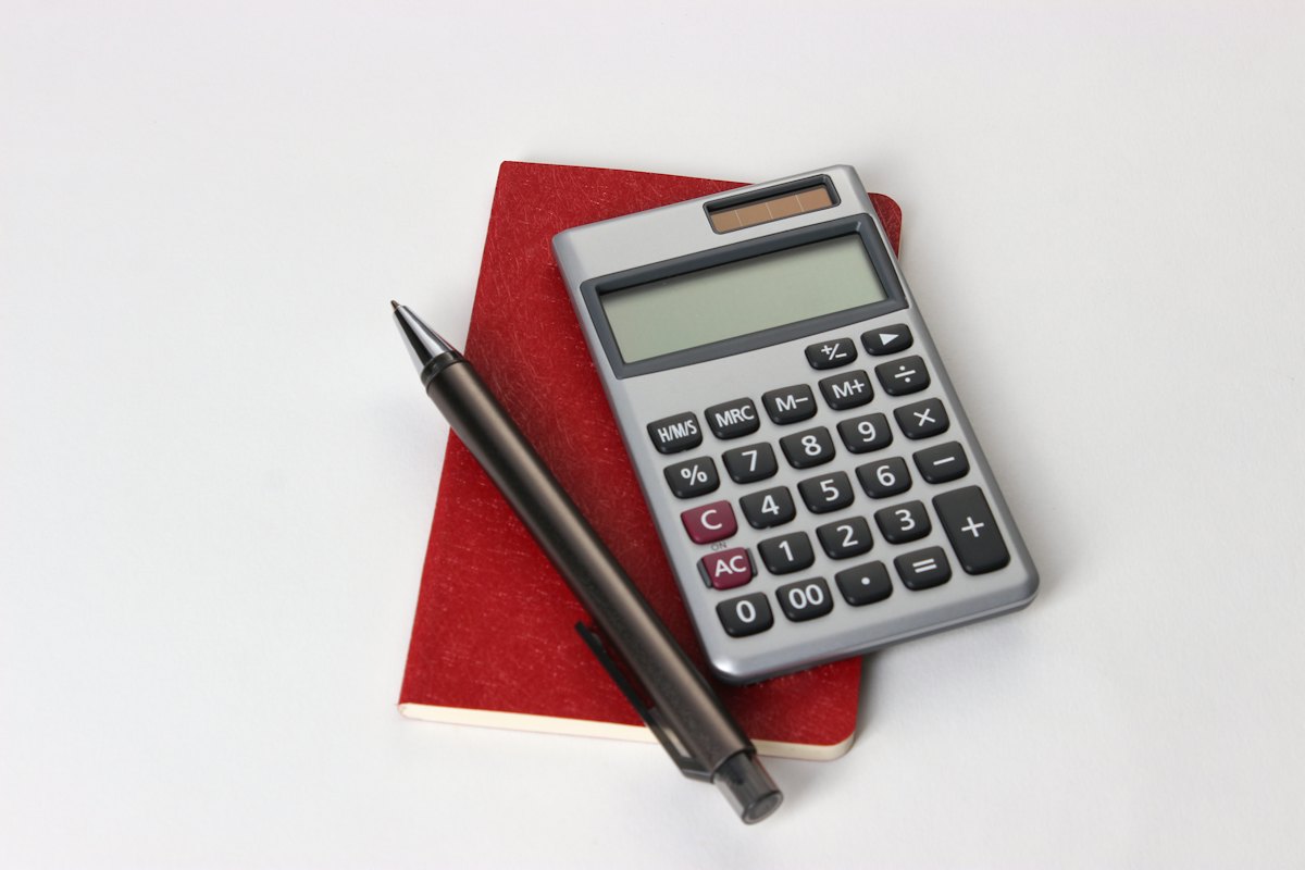A calculator and a pen on a red notebook