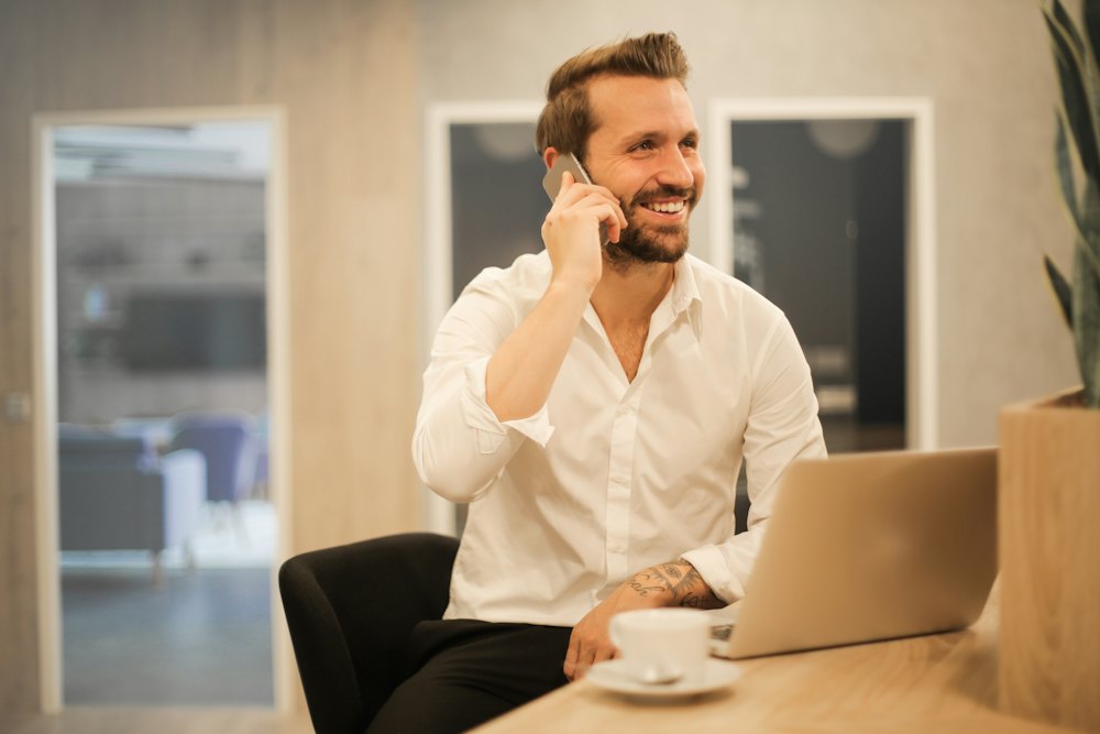 A man smiling while talking on the phone at his desk