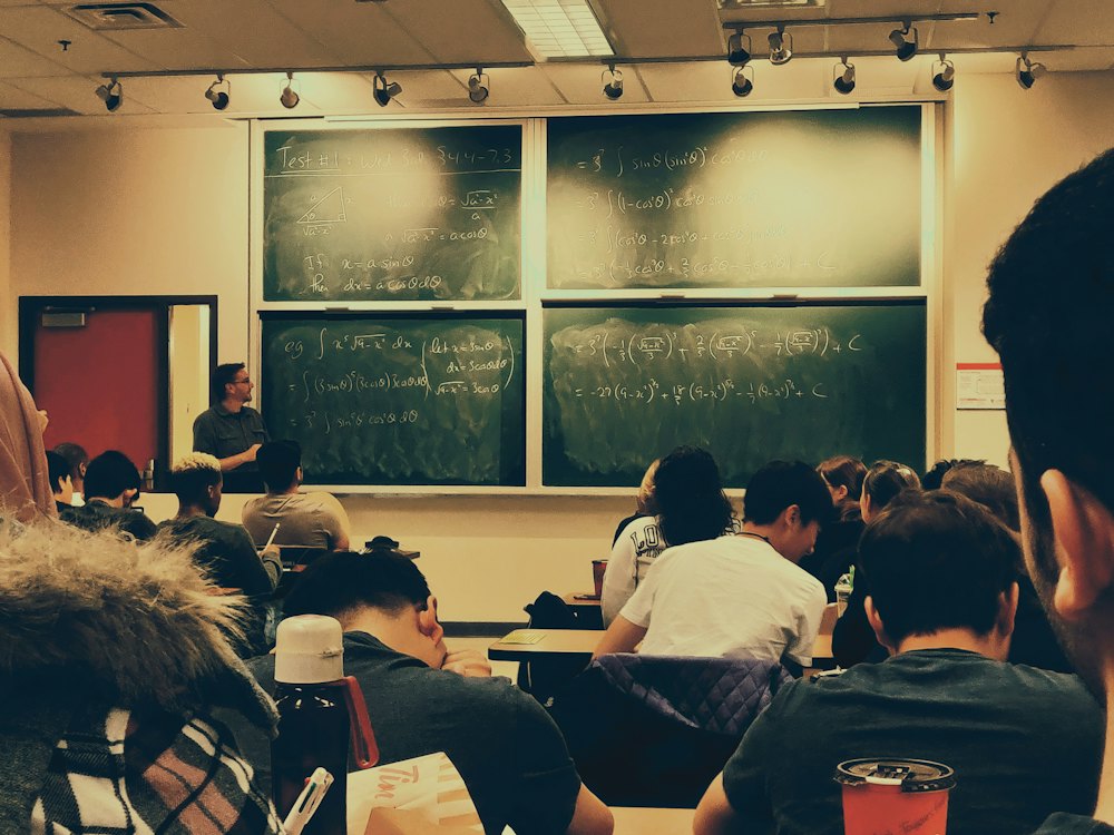 Adults sitting at desks in a classroom with a chalkboard