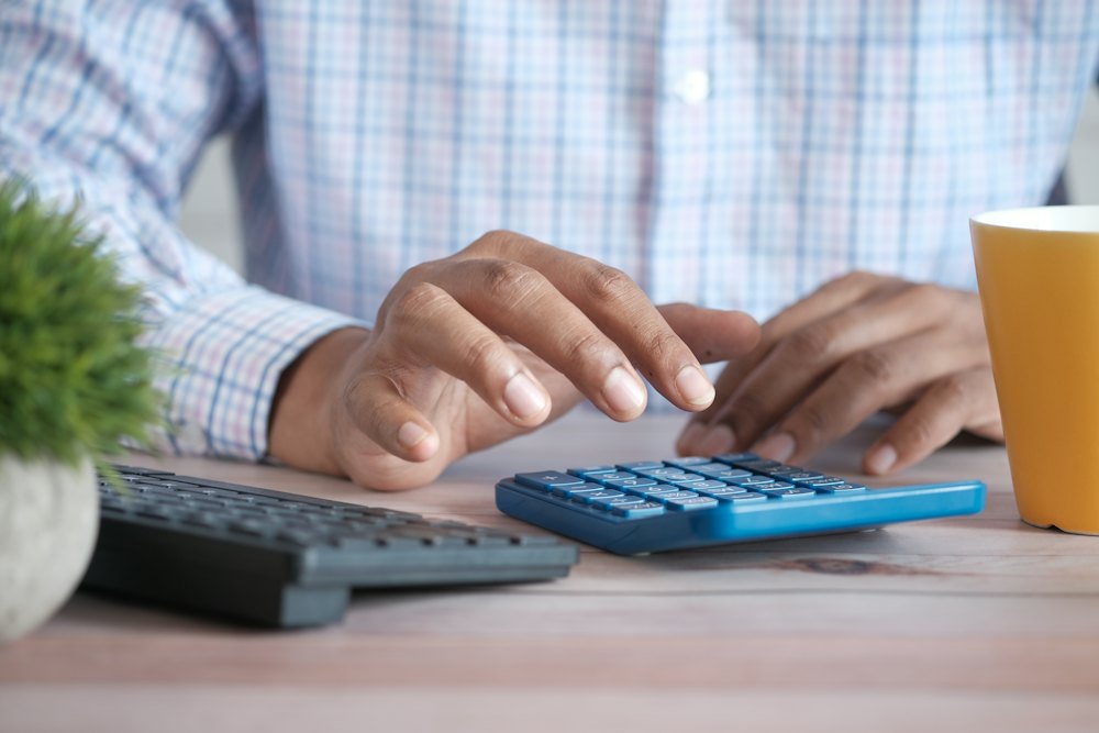 Hands working out sums on a calculator beside a laptop